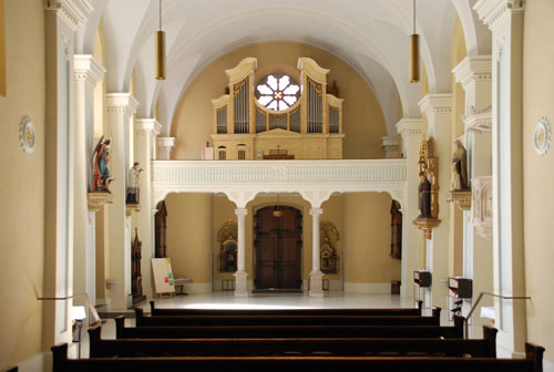L'aula della chiesa storica e la cantoria, ripresi dall'abside; in primo piano le panche della cappella feriale